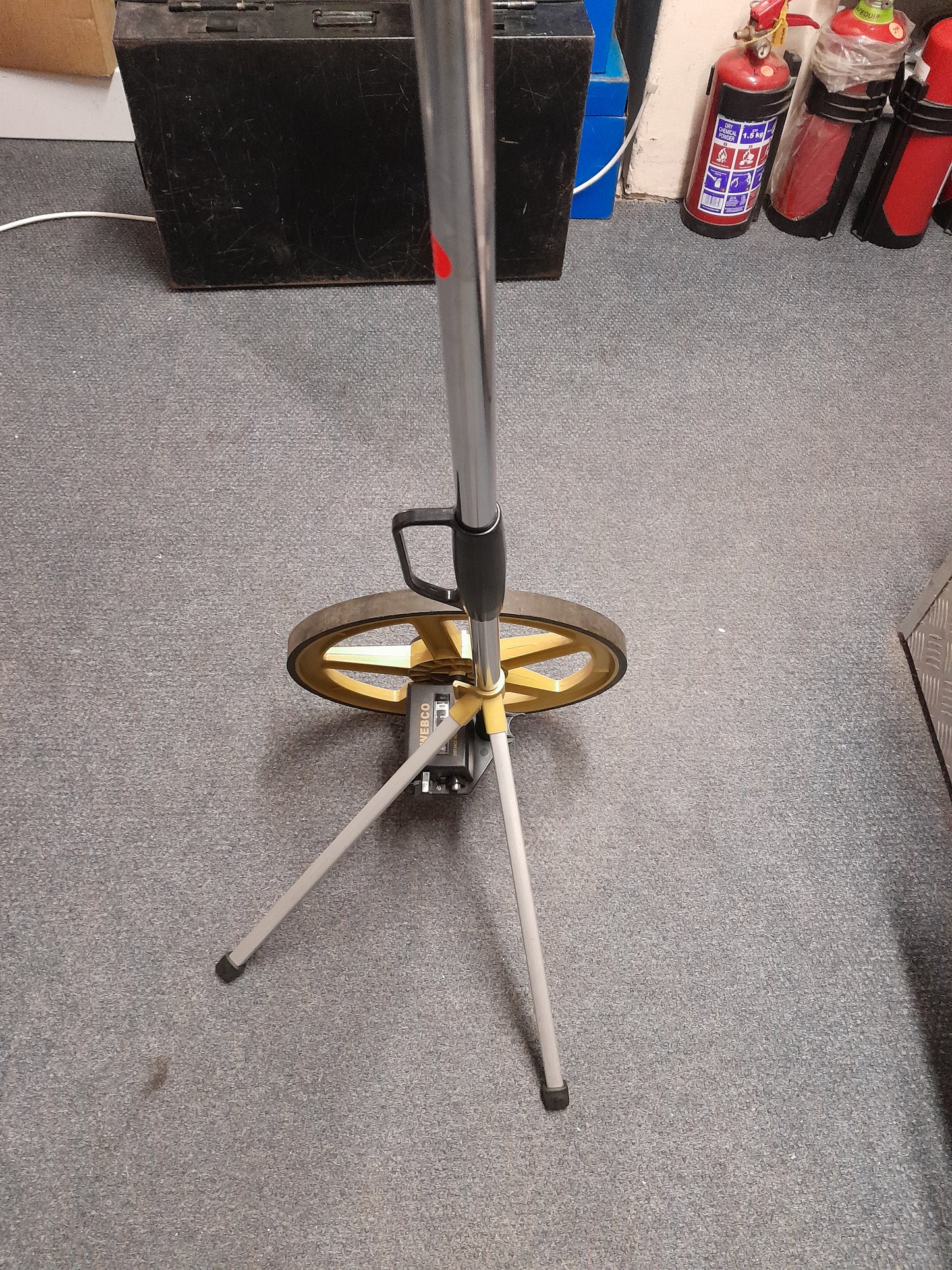 "Webco Distance Measuring Wheel with extended handle and yellow wheel on carpeted floor, used for precise distance measurements, available at Die Skatkis.