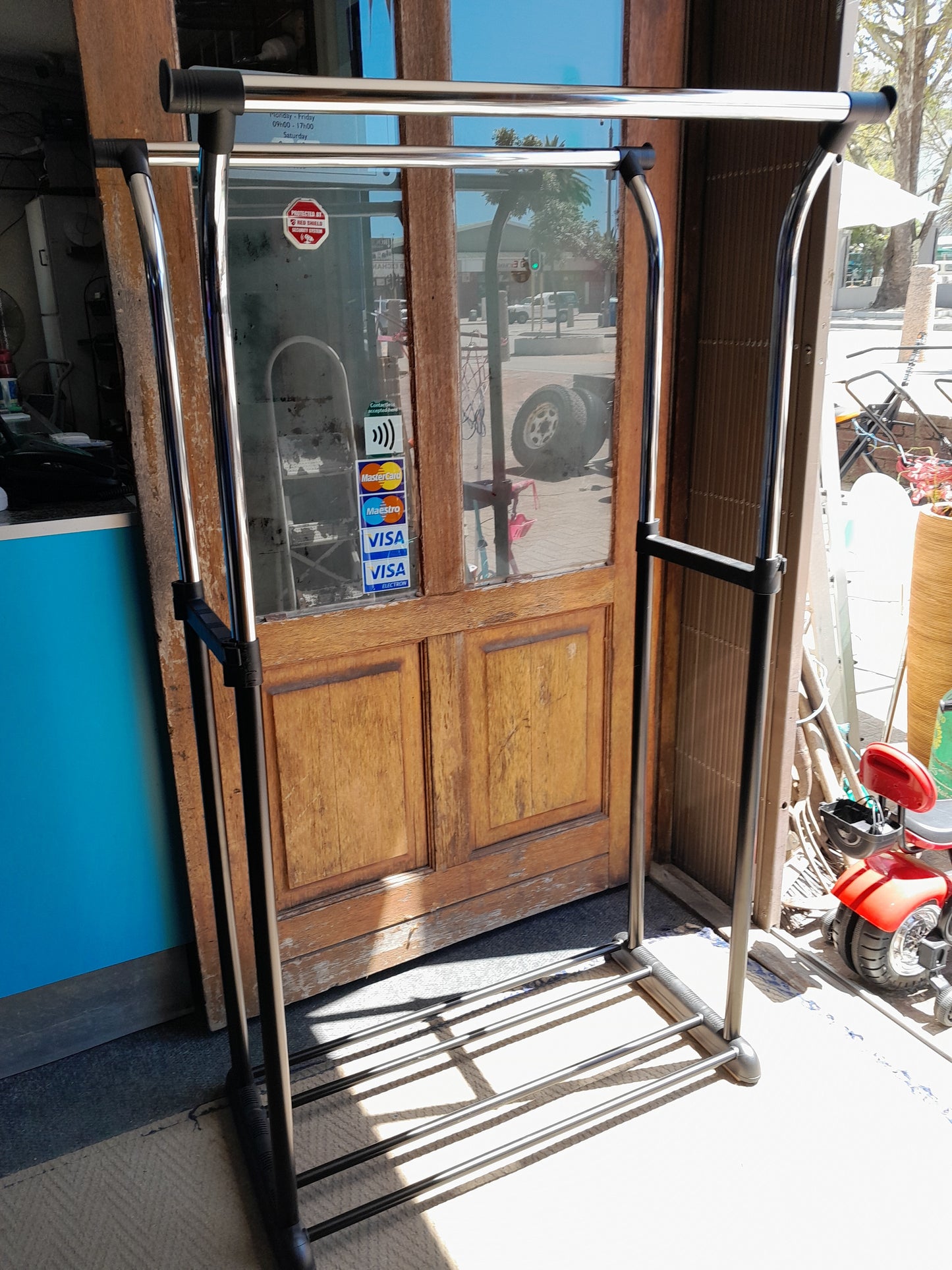 "Mainstays Double Adjustable Rolling Garment Rack, chrome finish, placed in front of a store entrance with payment stickers. Available at Die Skatkis.