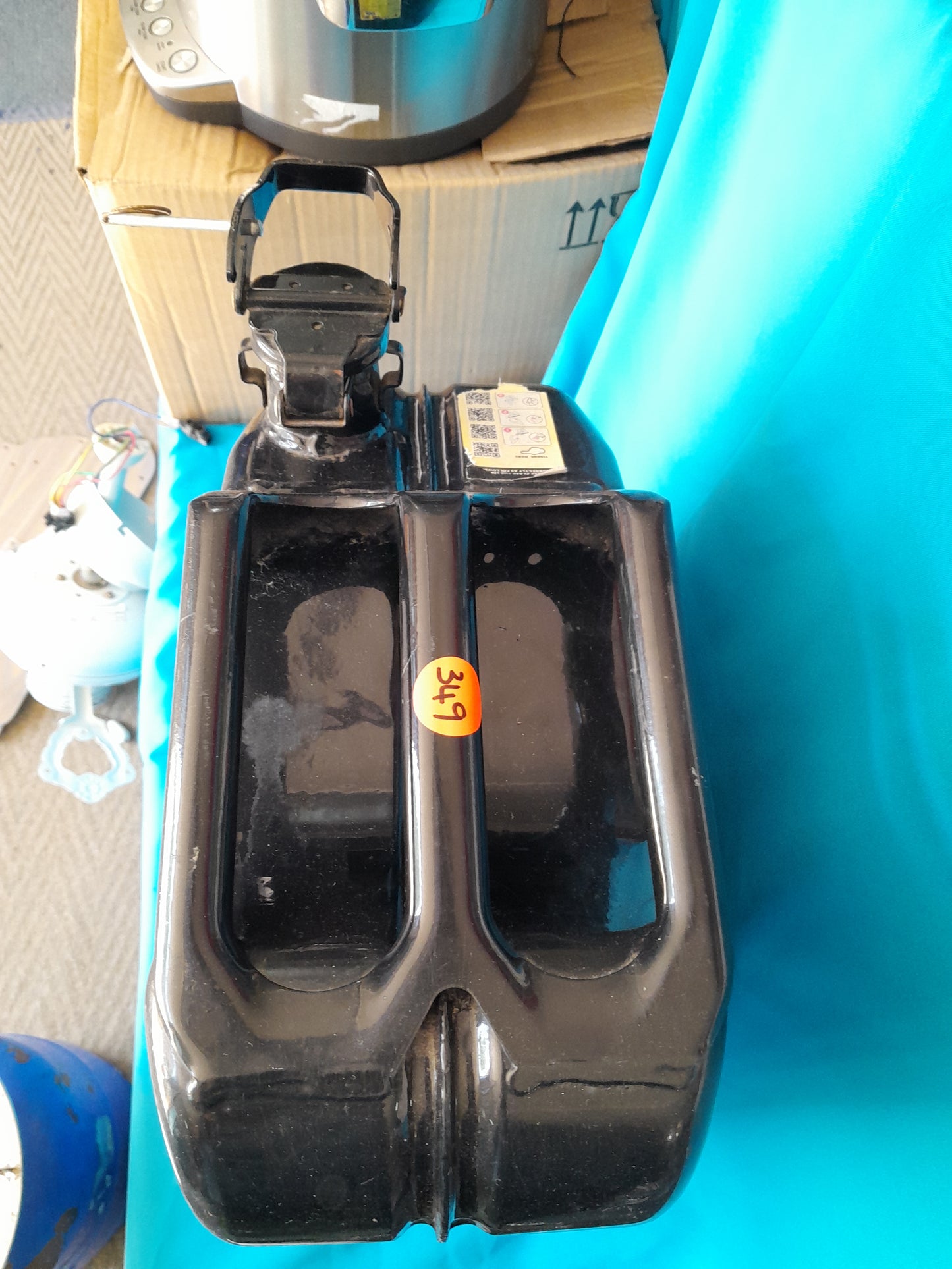 Black plastic container with handle and orange sticker labeled, on a blue surface, available at Die Skatkis.