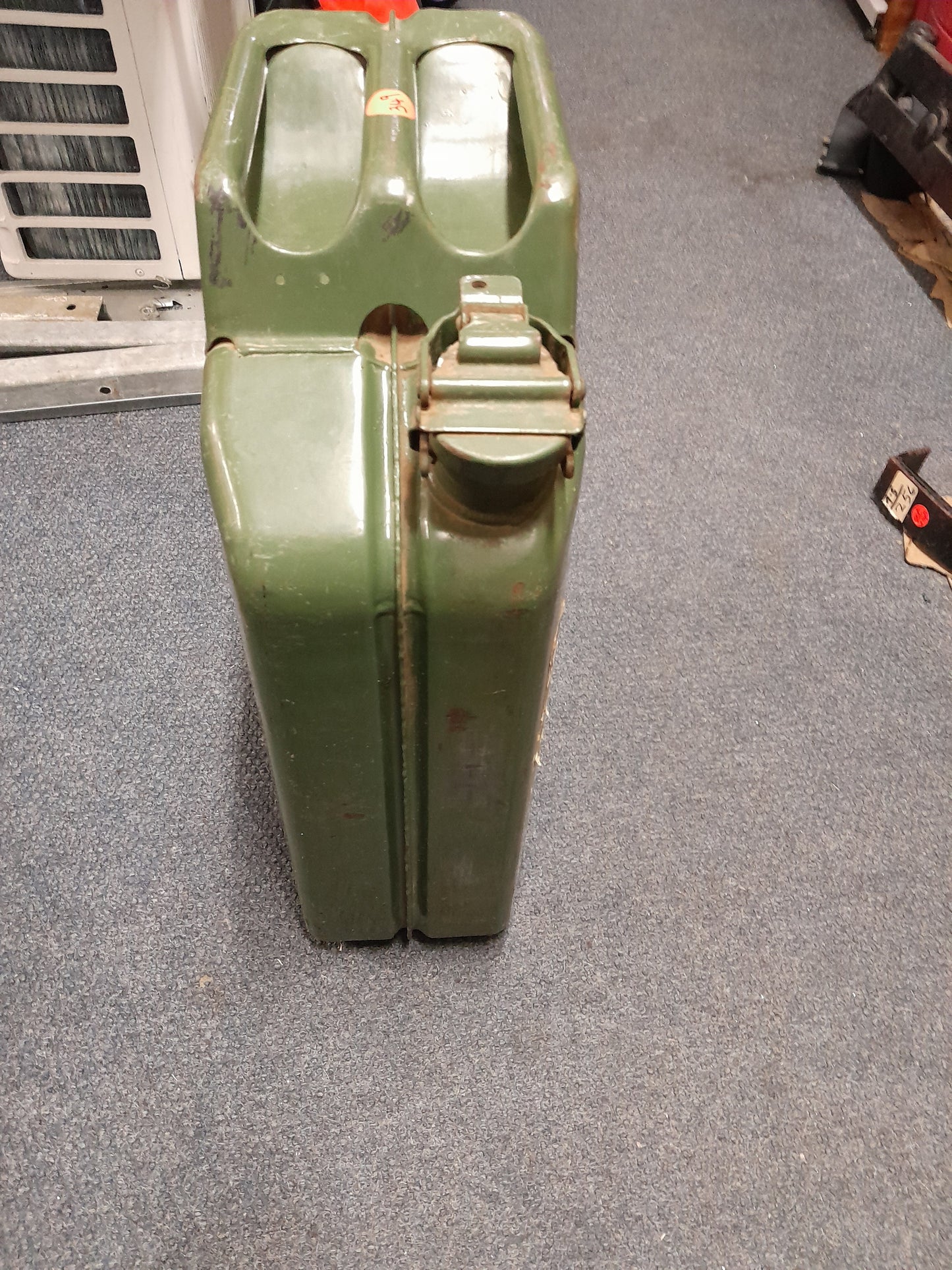 Green 20-liter military-style Jerry canister on the floor, ideal for storing and transporting liquids like fuel and water.