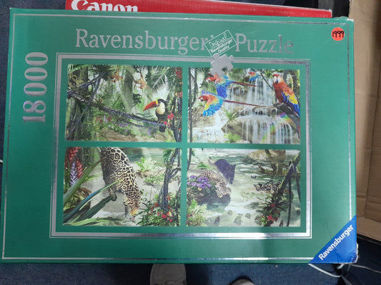 Ravensburger 18000 piece puzzle box featuring vibrant rainforest scenes with toucans, macaws, and jaguars. Available at Die Skatkis.