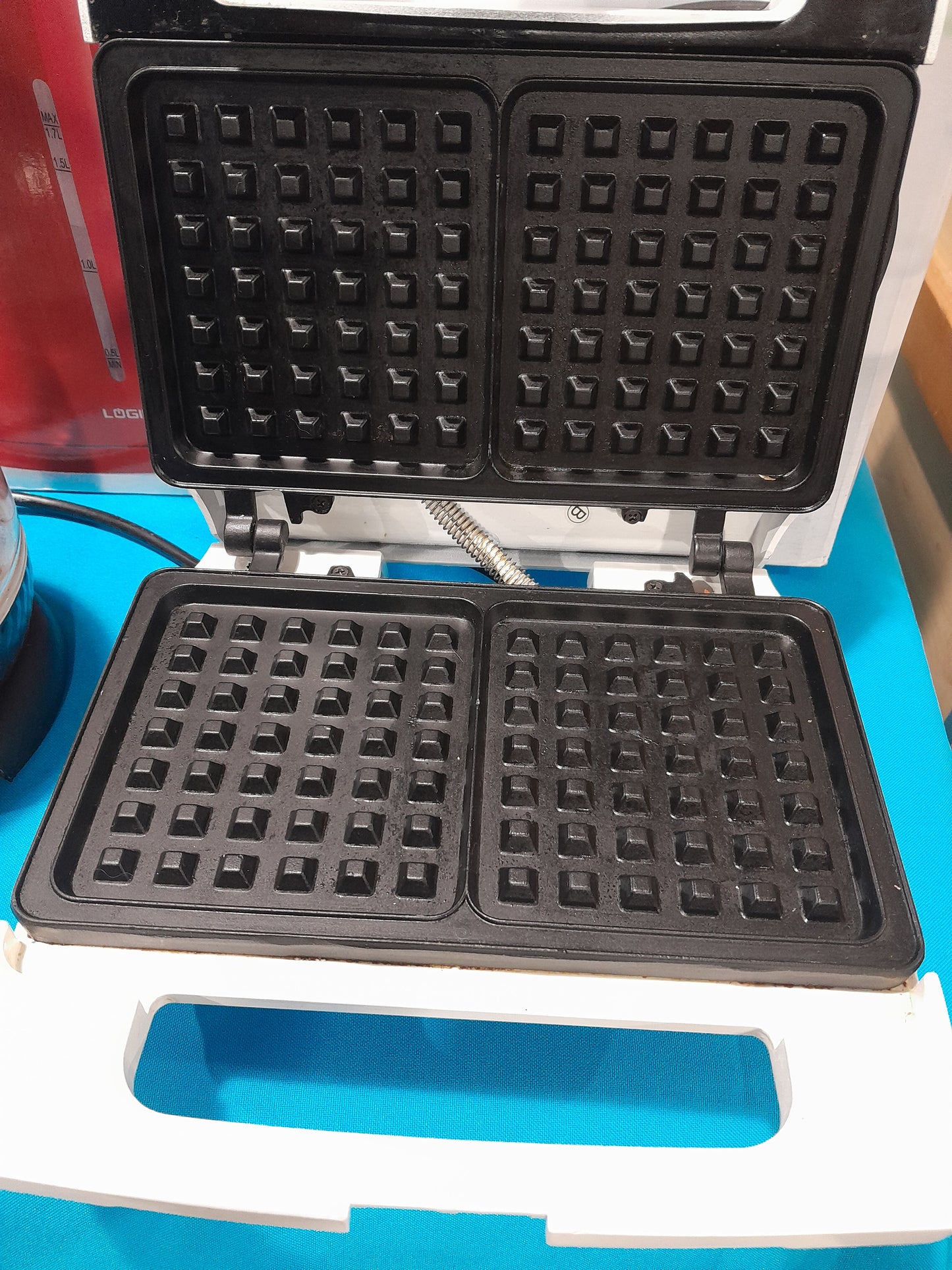 Logik waffle maker displayed on a blue background, showcasing its sleek design.