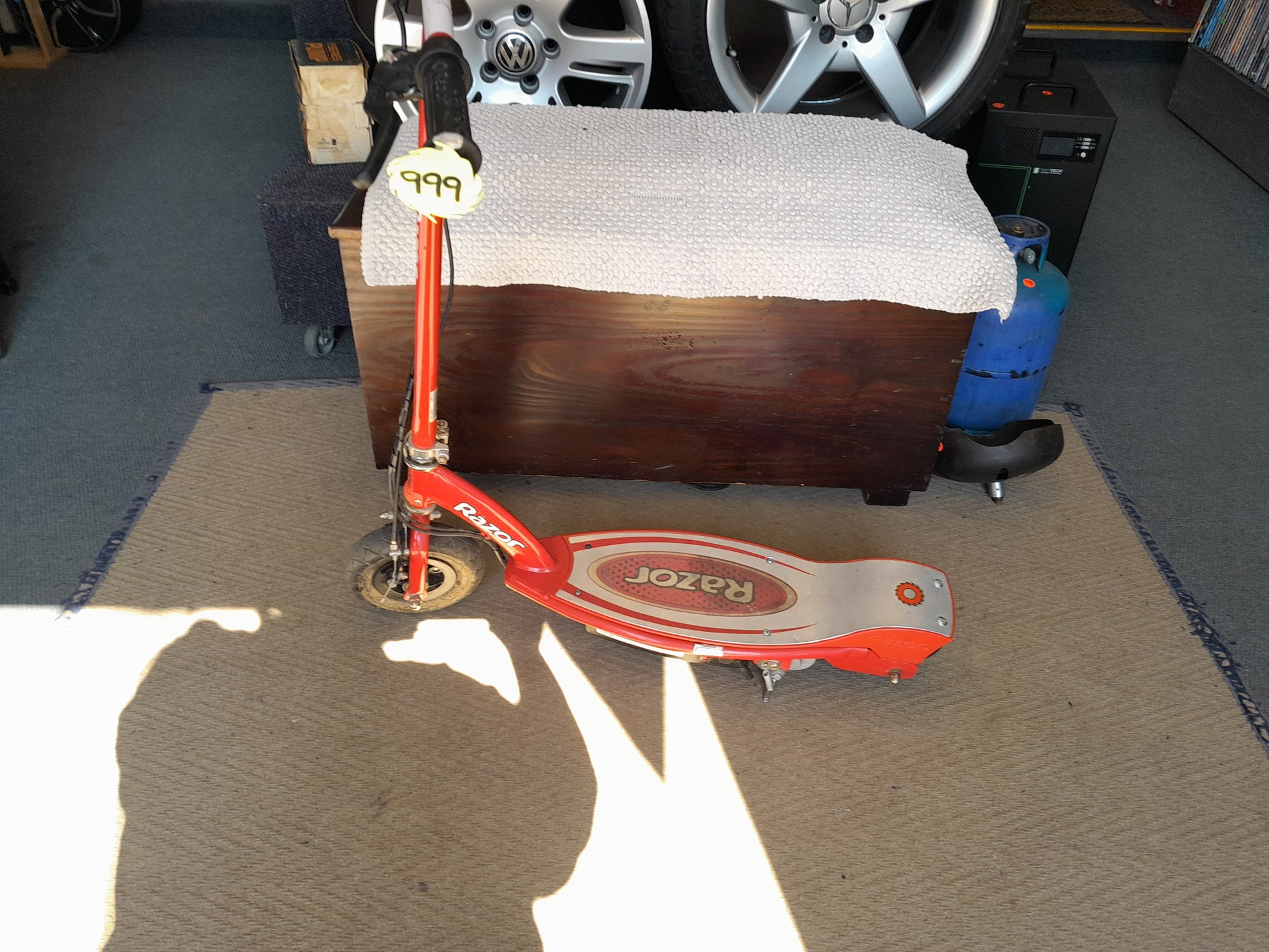 Red Razor E90 electric scooter with a price tag of 999, showcased on beige carpet in a garage, available at Die Skatkis.