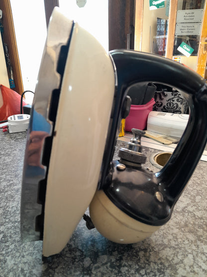 Vintage Tilley Kerosene Iron with a black handle and beige body, displayed on a countertop among various items, available at Die Skatkis.