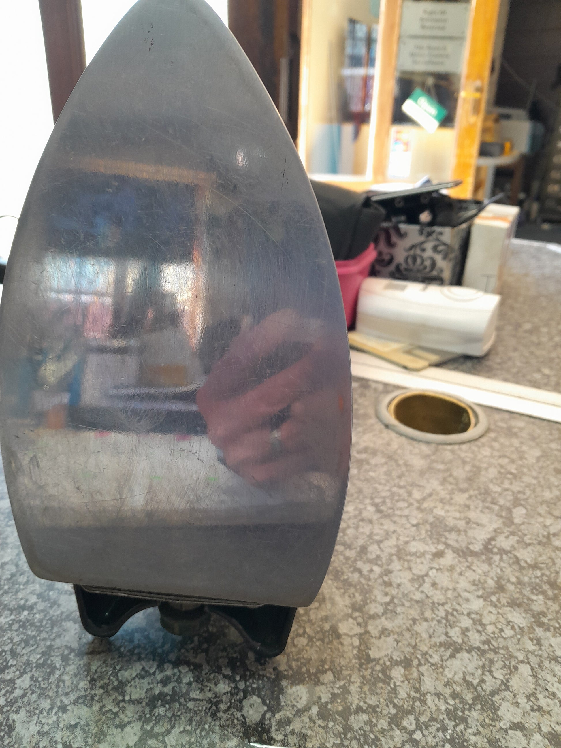 Slightly scratched soleplate of a Vintage Tilley Kerosene Iron, reflective surface on countertop among various items, available at Die Skatkis.