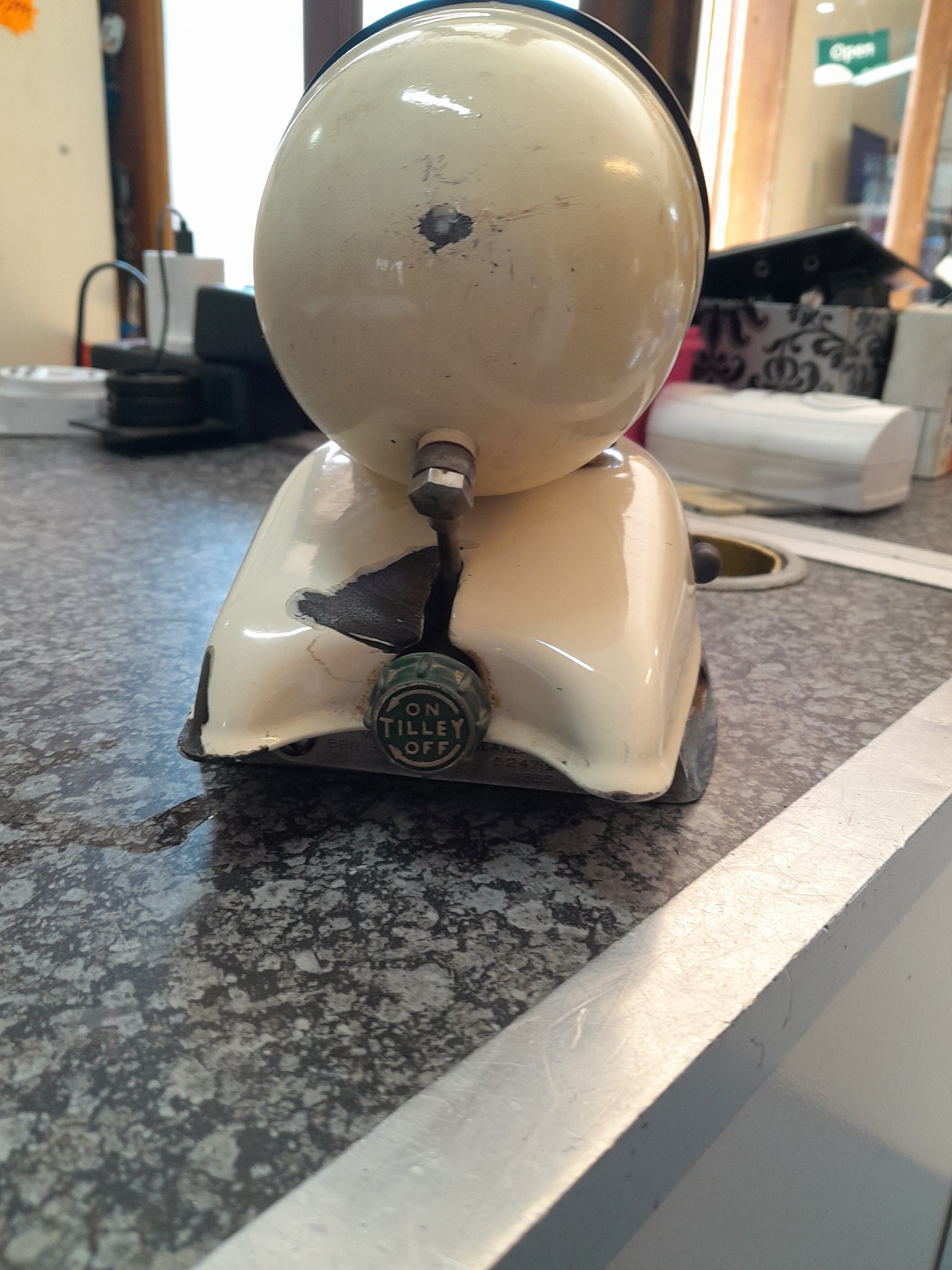 Close-up of a damaged vintage Tilley Kerosene Iron with a green knob, visible crack at its base, displayed on a speckled countertop, available at Die Skatkis.