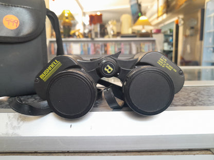 Close-up of Bushnell 7x35 binoculars with lens caps on, text showing 420 FT. AT 1000 YDS. 140 M AT 1000 M FIELD 6º, available at Die Skatkis.