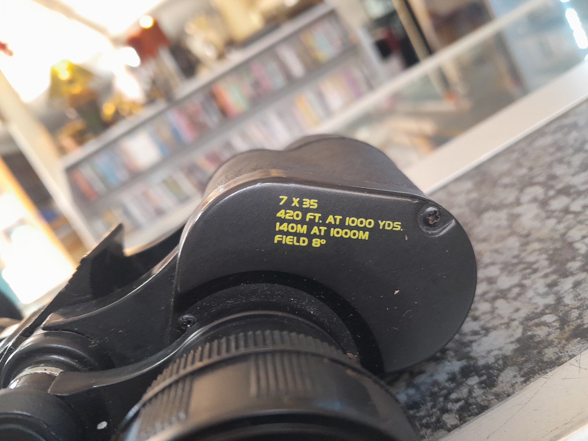 Close-up view of Bushnell 7x35 binoculars, text showing 420 FT. AT 1000 YDS. and 140M AT 1000M FIELD 6º, available at Die Skatkis.
