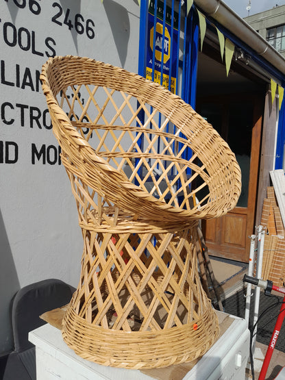 Handwoven wicker chair with wide, open-weave design, placed outdoors in front of a store. Available at Die Skatkis.