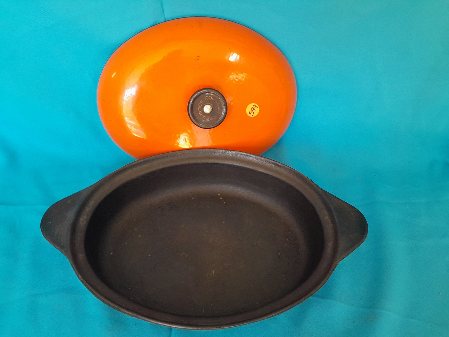 Orange cast iron oval casserole pot with black interior and handles, lid with black knob, available at Die Skatkis.