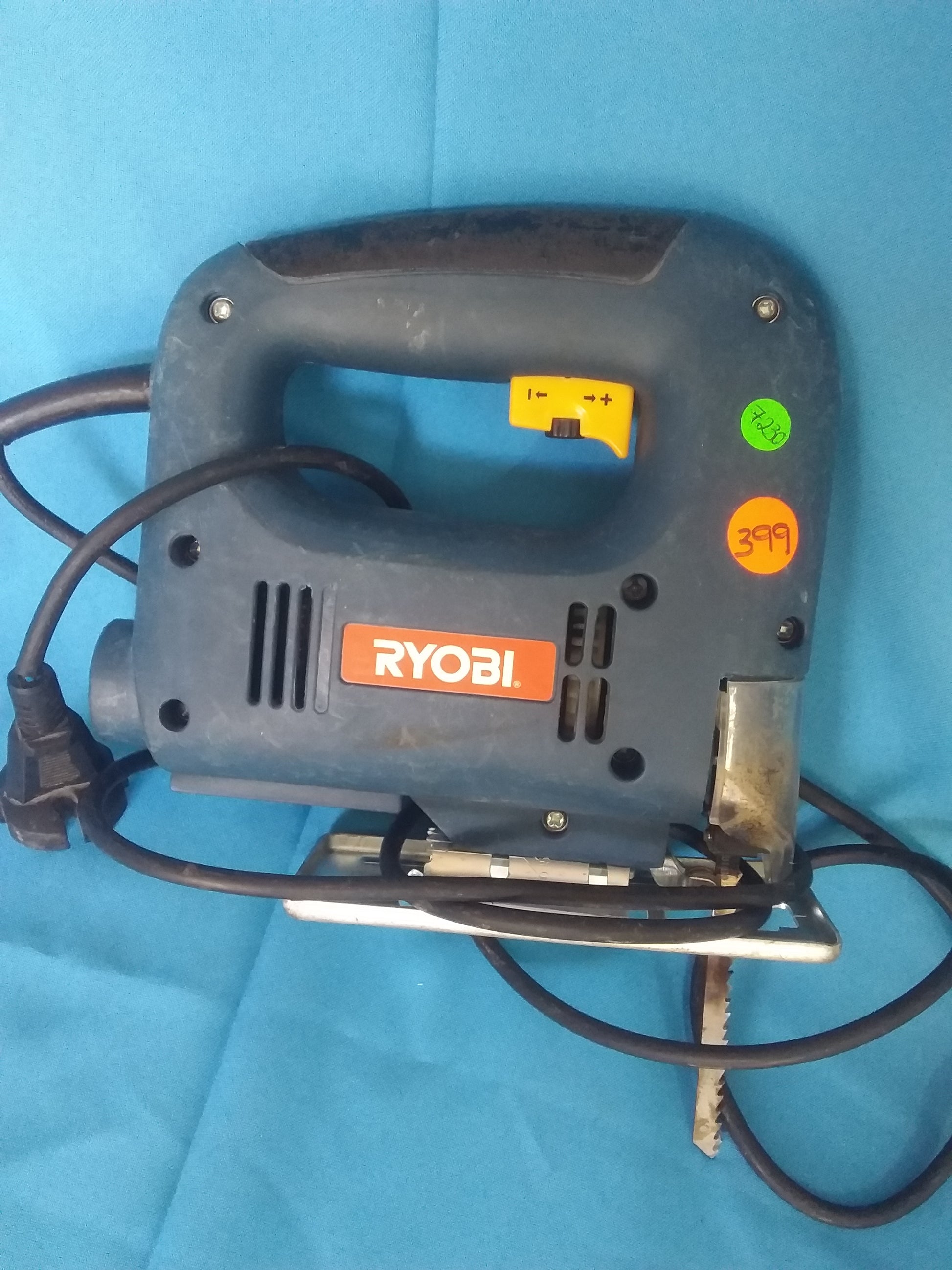 Ryobi jigsaw with black handle, speed control switch, and power cord, on blue surface, available at Die Skatkis.