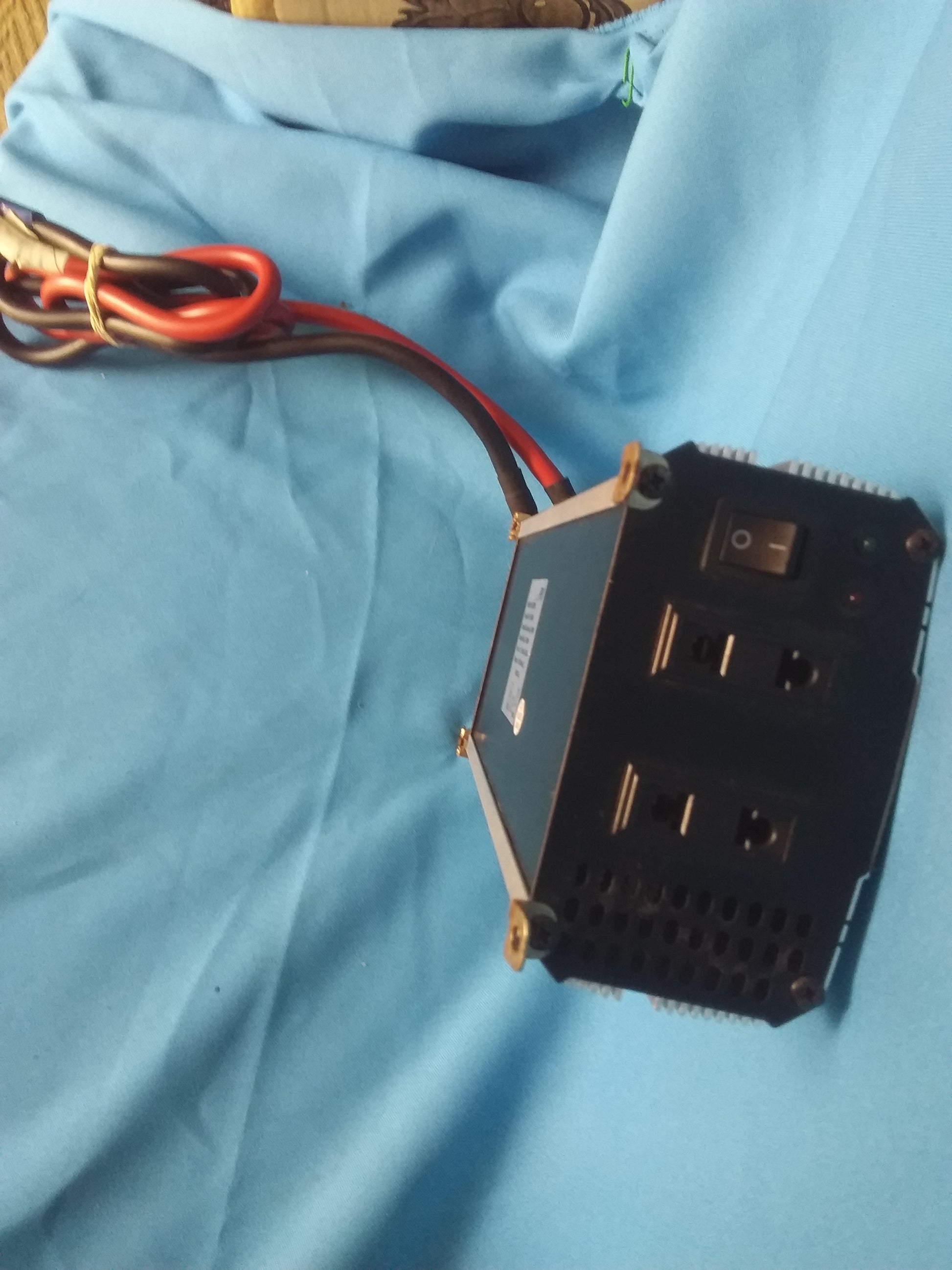 "ProUser power inverter with two electrical outlets, on/off switch, red and green indicator lights, and ventilation holes, placed on blue fabric.