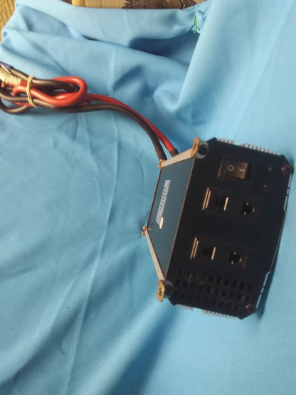"ProUser power inverter with two electrical outlets, on/off switch, red and green indicator lights, and ventilation holes, placed on blue fabric.