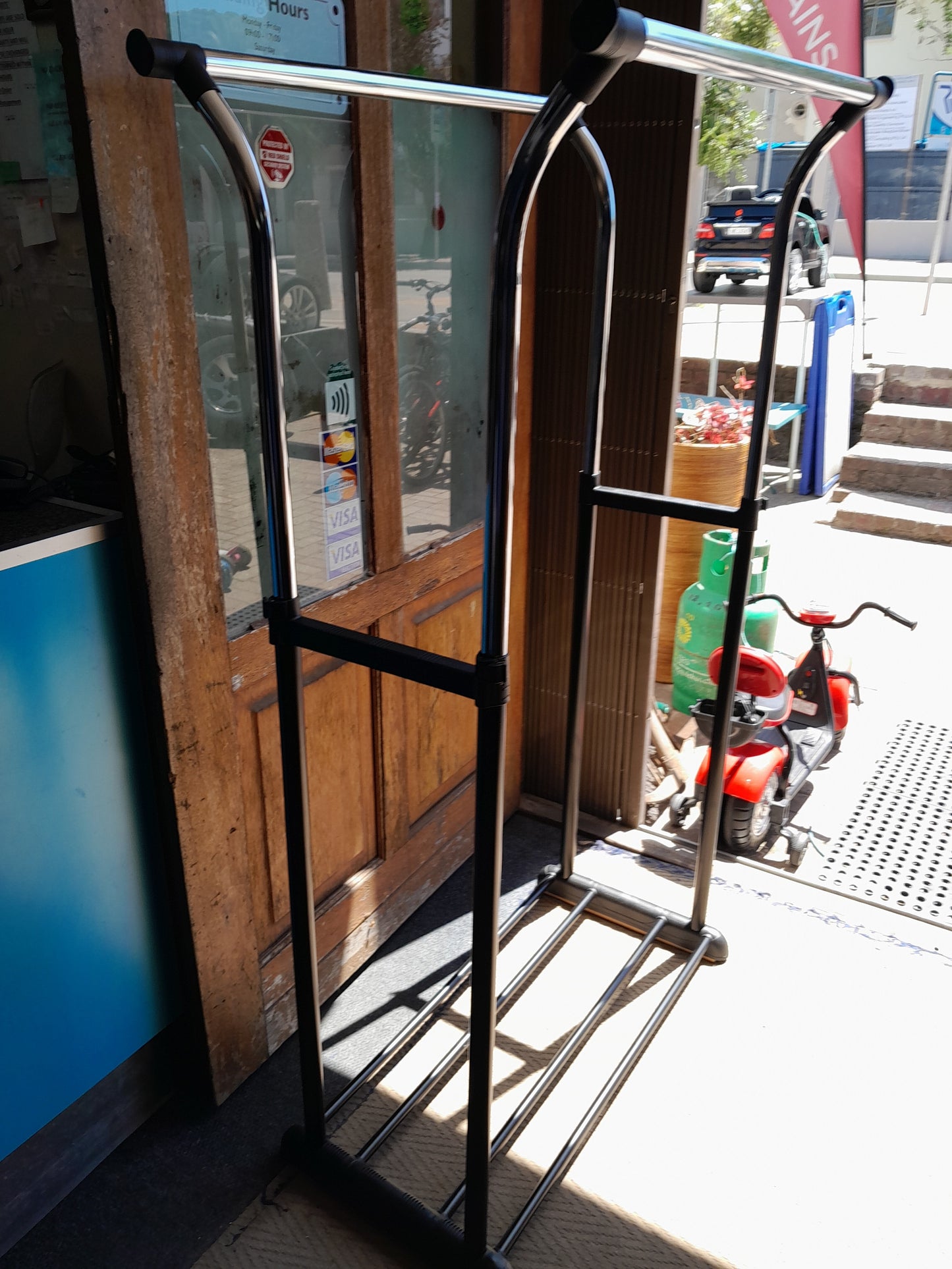 Metal frame structure, likely an exercise equipment, near a door with glass panels. Various items in the background. Available at Die Skatkis.