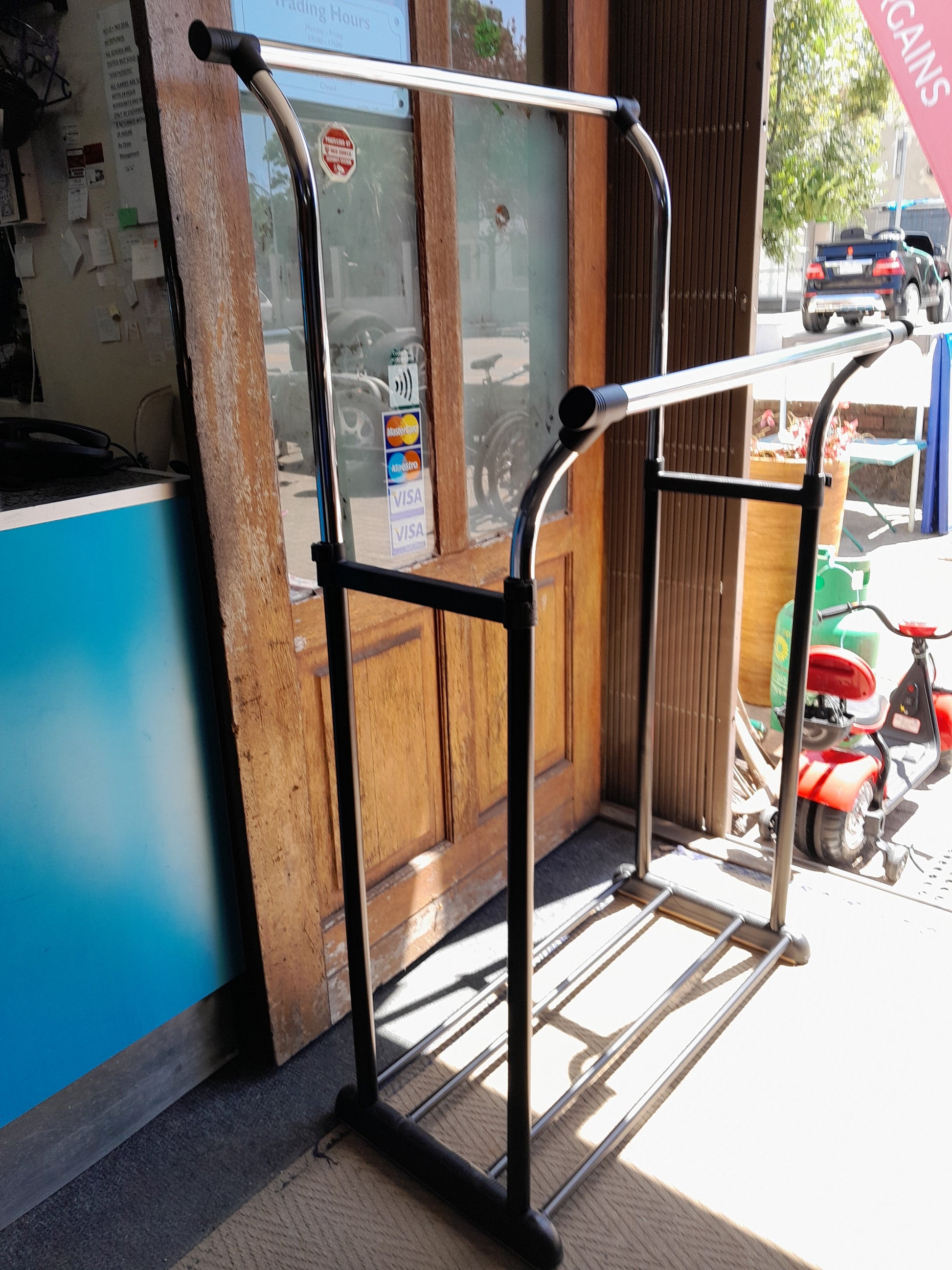 Secondhand metal garment rack, black and silver, in front of a door with payment method stickers. Find it at Die Skatkis.