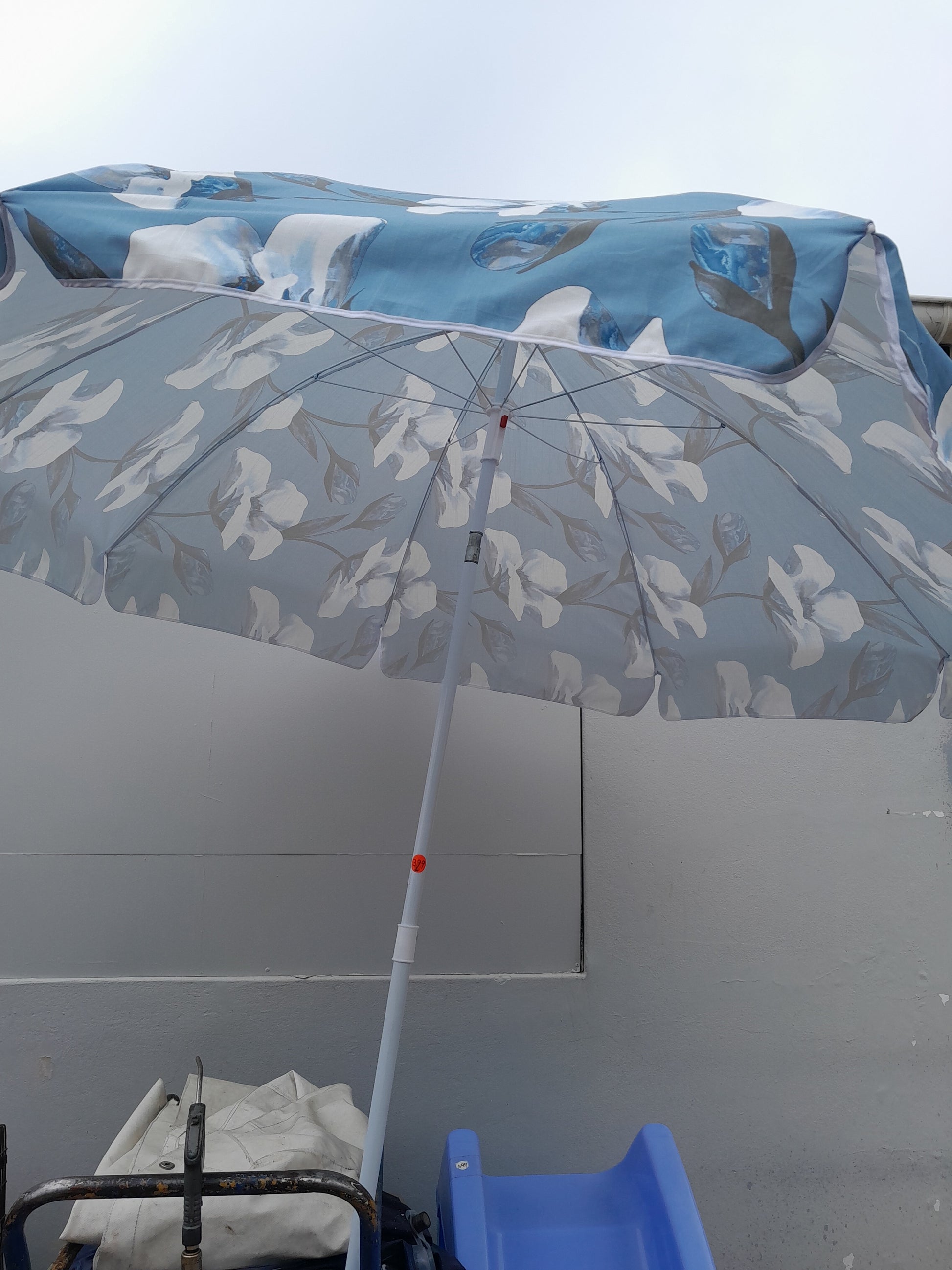 "200 cm Design House umbrella, Maldives model, featuring a blue and white flower design. Open and shown with other items beneath. Available at Die Skatkis.