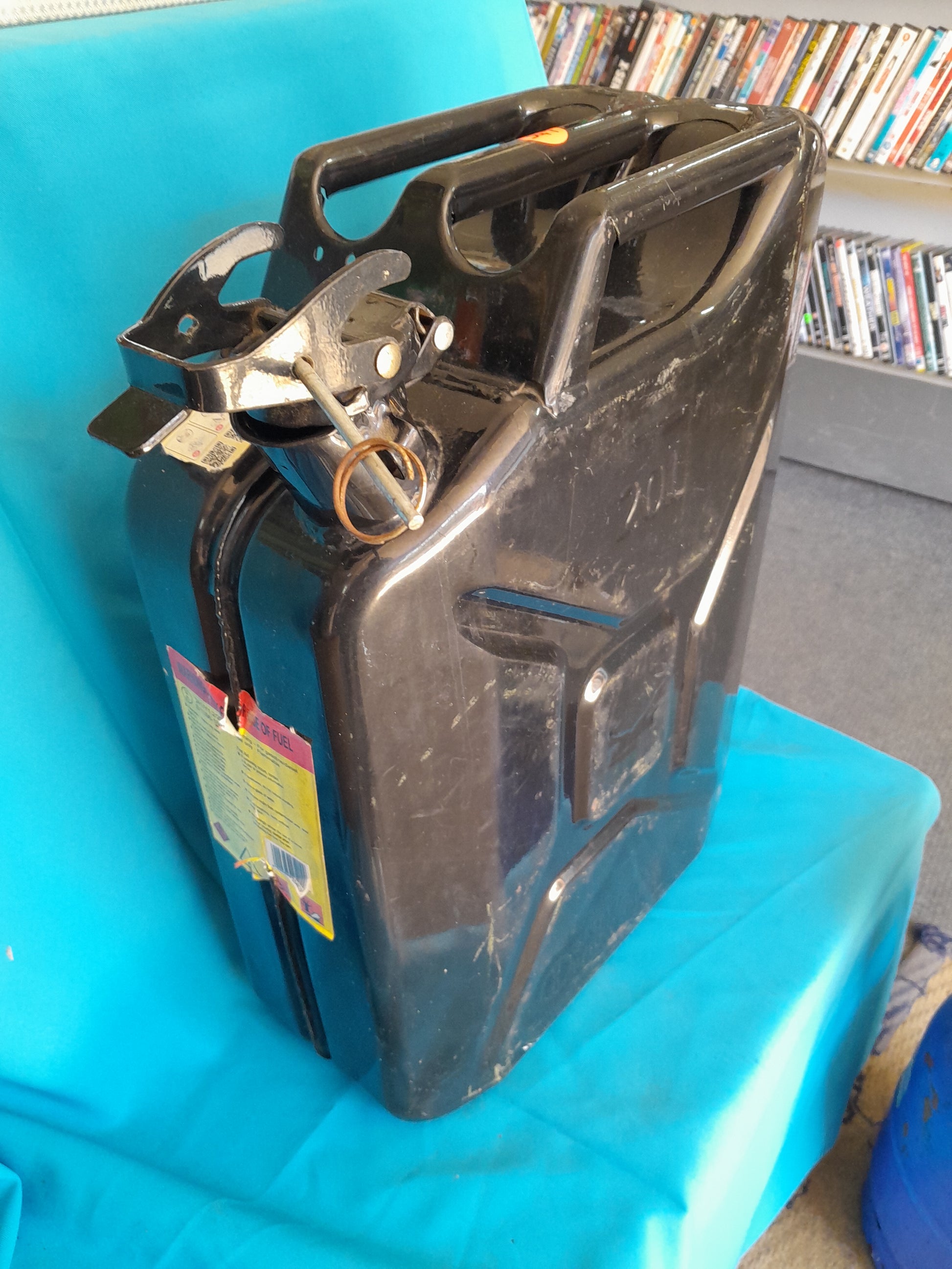 Black 20L Jerry can with a handle and secure spout, placed on a blue fabric surface, ideal for storing fuel, available at Die Skatkis.