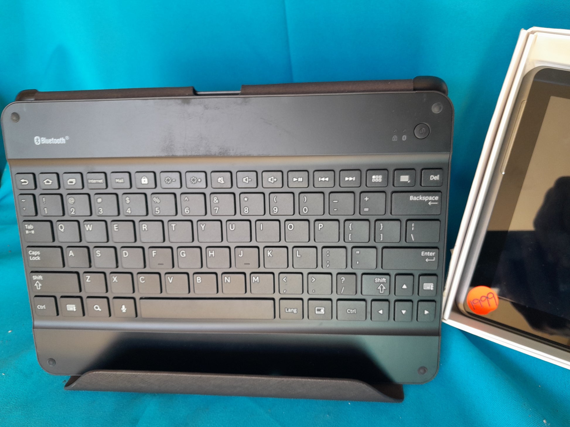 Bluetooth keyboard with full QWERTY layout and Samsung Galaxy Tab 2 10.1 with price tag, displayed on blue fabric, available at Die Skatkis.