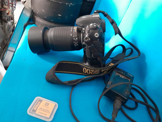 Nikon D200 camera setup including lens, battery, charger, and memory card on a blue surface.