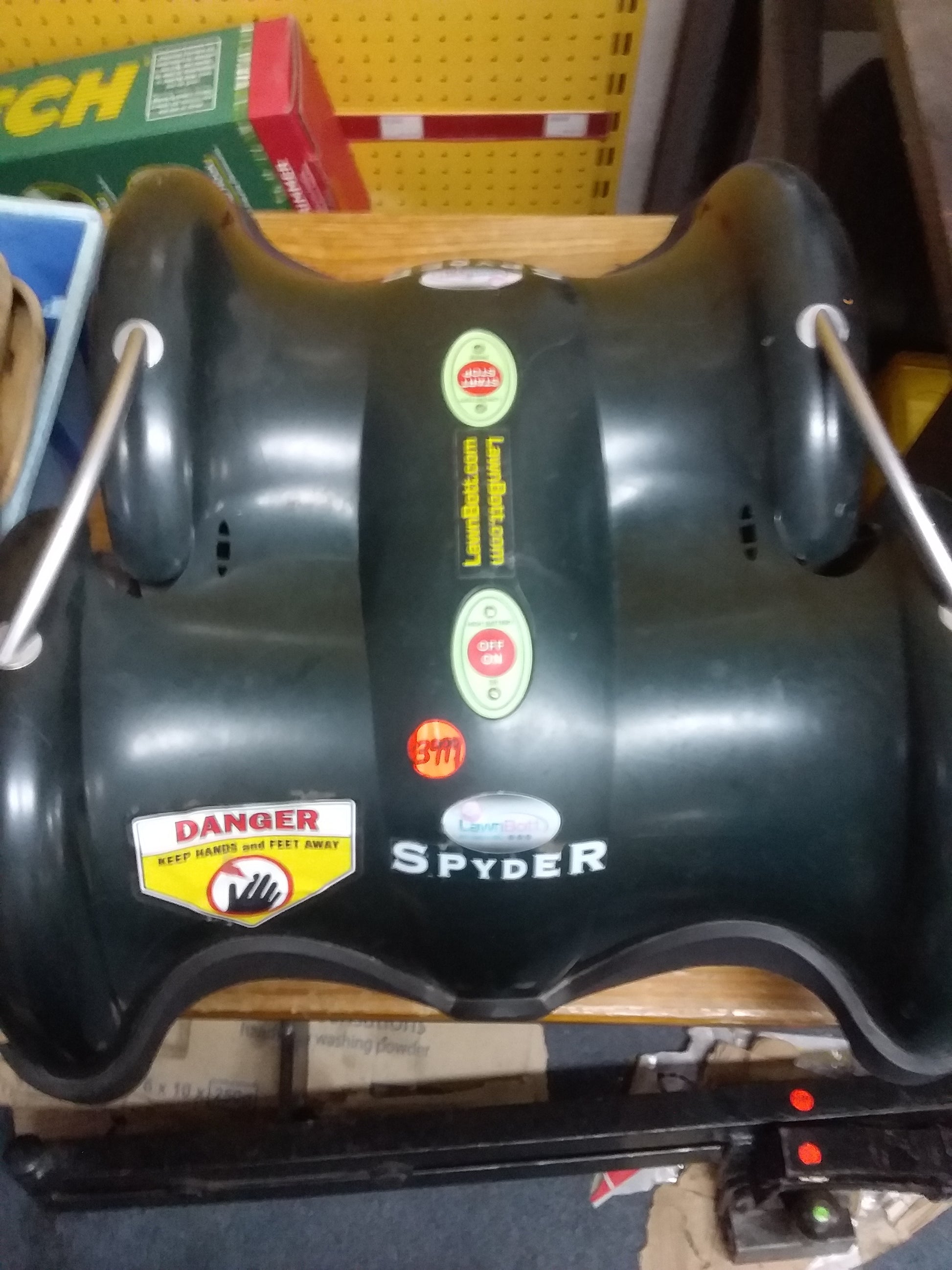 "LawnBot Spyder robotic lawnmower with safety labels, green control buttons, and LawnBot.com branding. Available at Die Skatkis.