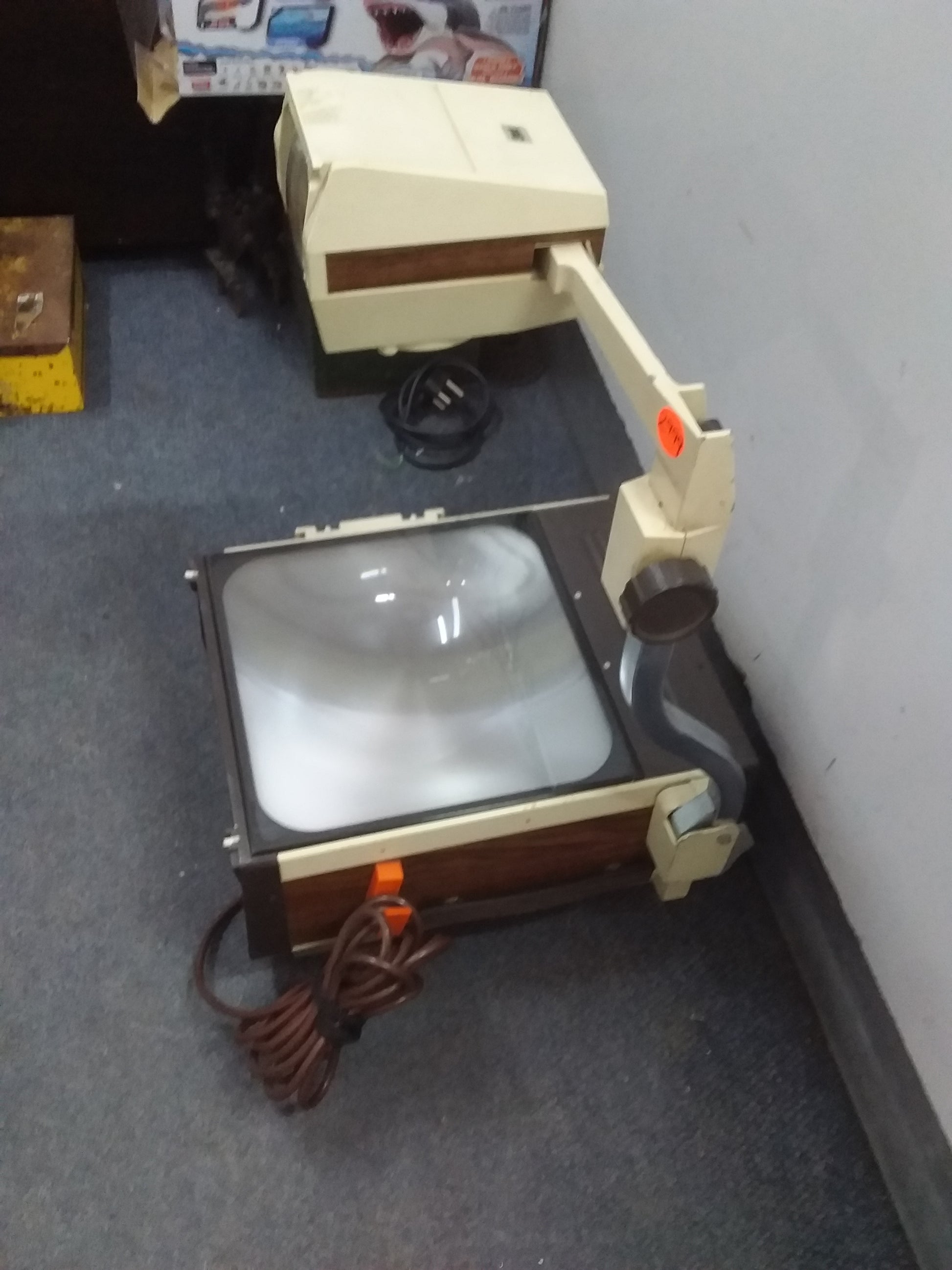 "Beige vintage 3M overhead projector, model 213, with brown accents and a coiled power cord, displayed on a tiled floor. Available at Die Skatkis.