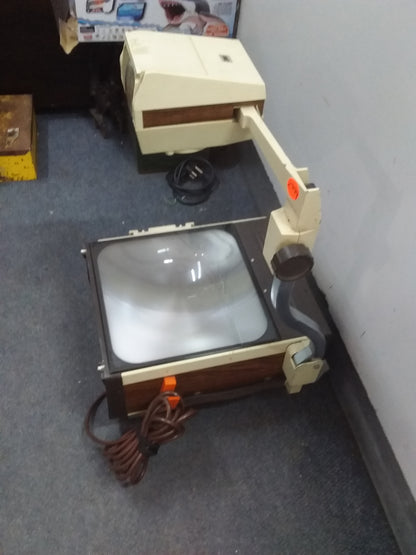 "Beige vintage 3M overhead projector, model 213, with brown accents and a coiled power cord, displayed on a tiled floor. Available at Die Skatkis.