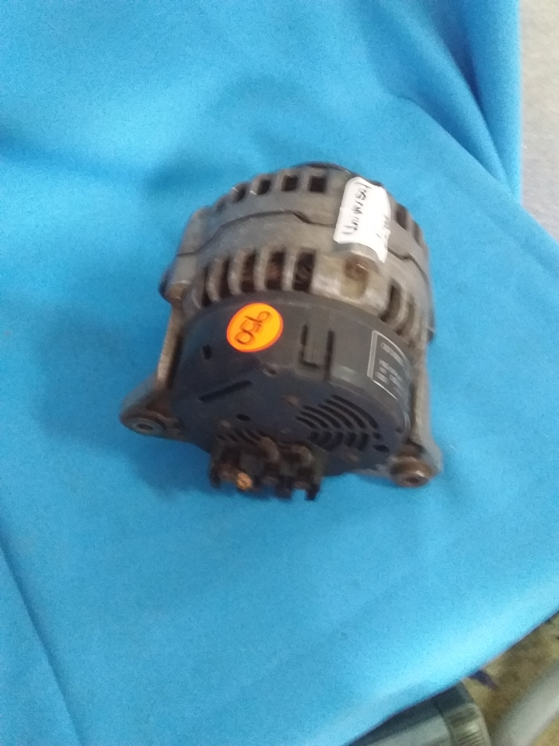 Universal Ford alternator with label marked 'V5M1' and orange sticker '950,' placed on a blue surface. Available at Die Skatkis.