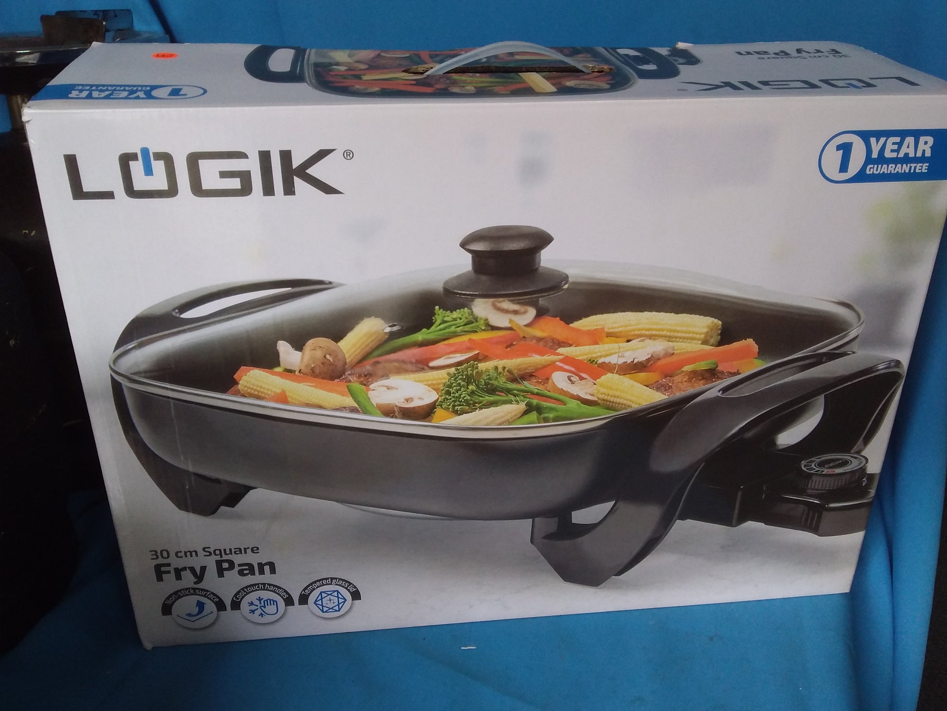 Logik 30cm square fry pan with non-stick surface and tempered glass lid, shown in original packaging with 1-year guarantee. Available at Die Skatkis.