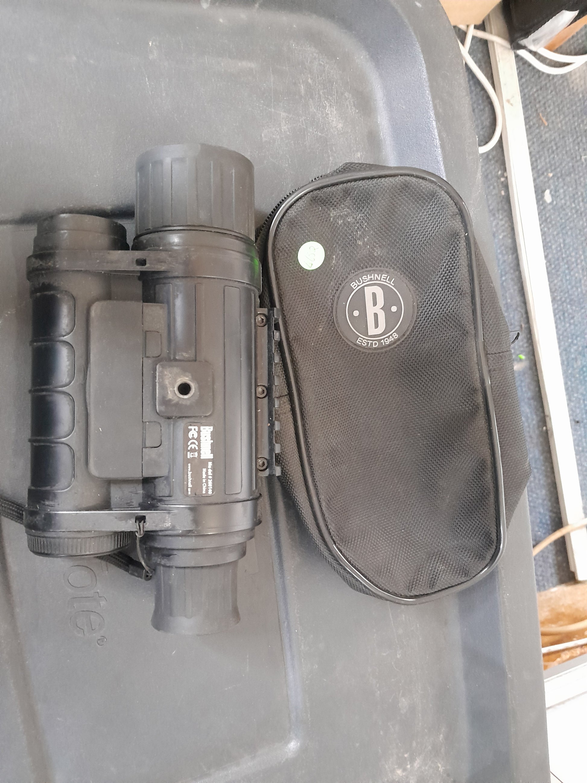 "Bushnell Equinox Z night vision device and carrying case with Bushnell logo, placed on a black surface. Available at Die Skatkis.