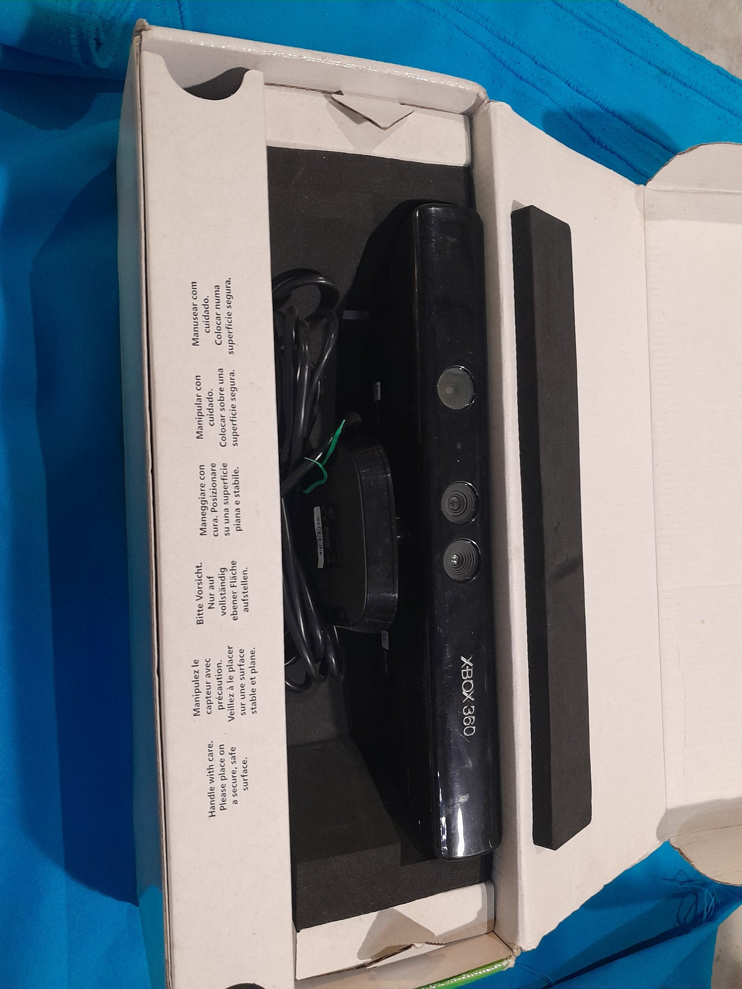 Open box of Xbox 360 Kinect sensor, displaying the device and included accessories.