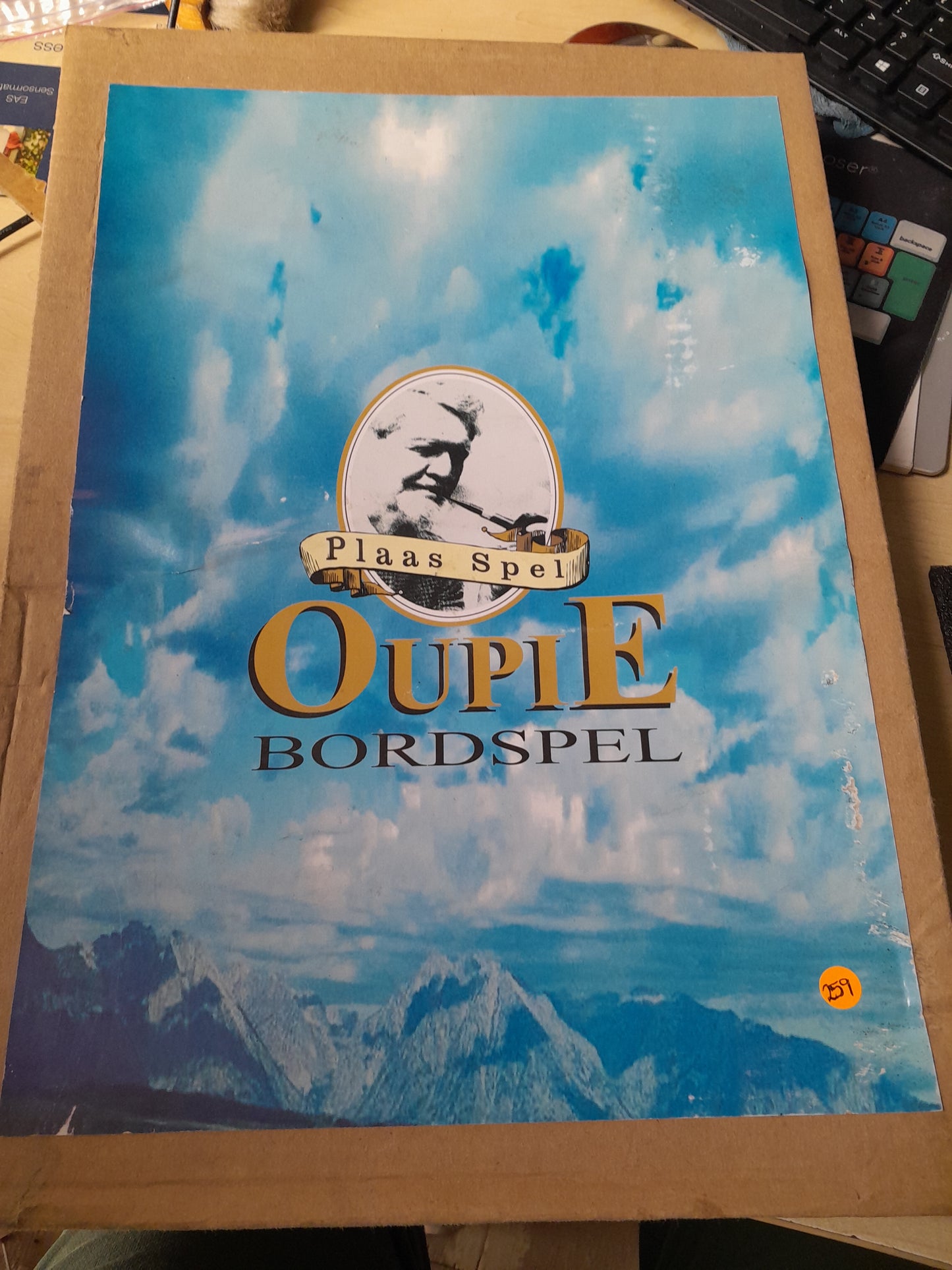 Oupie Bordspel board game box cover featuring scenic mountains and blue sky.